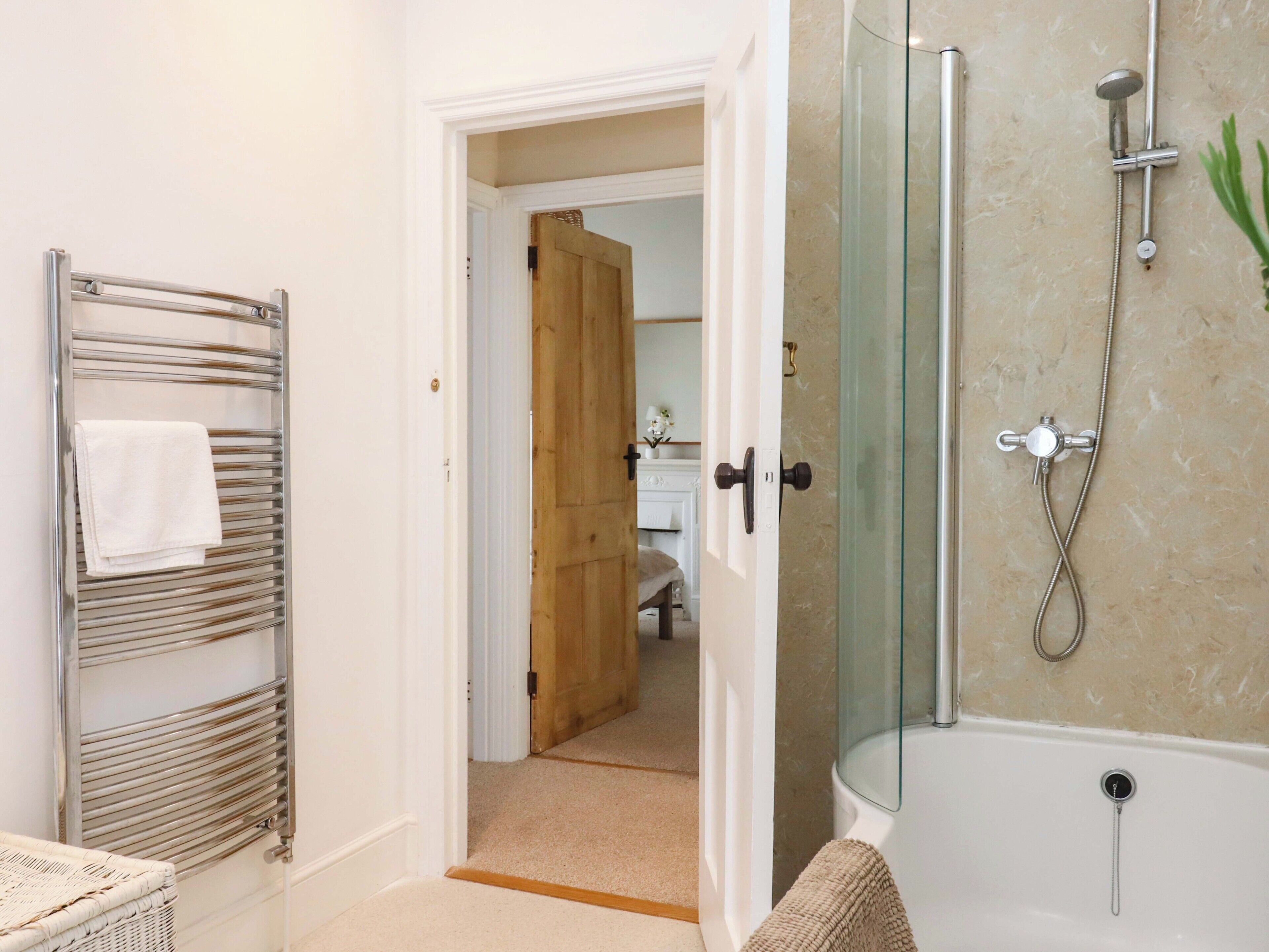 A bathroom with a glass-enclosed shower, a towel rack, and a wicker basket.