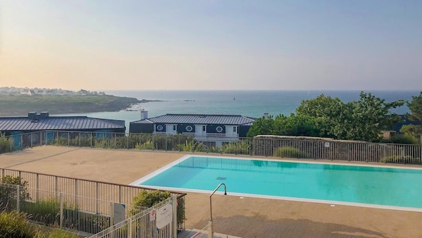 A swimming pool with a view of the sea, surrounded by buildings with a metal roof. - Family Escape near Trescadec (Audierne)