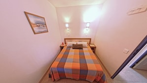 A small hotel room with a checkered bedspread, two bedside lamps, a nightstand, a framed picture on the wall, and a tiled floor. - Family Escape near Trescadec (Audierne)
