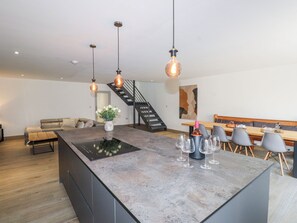 Una cocina moderna con una isla central, luces colgantes, una escalera y un comedor con sillas y una mesa.