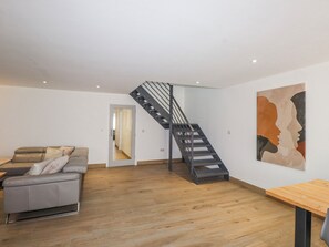 Una sala de estar moderna con un sofá gris, suelo de madera, una escalera y un cuadro abstracto grande en la pared.