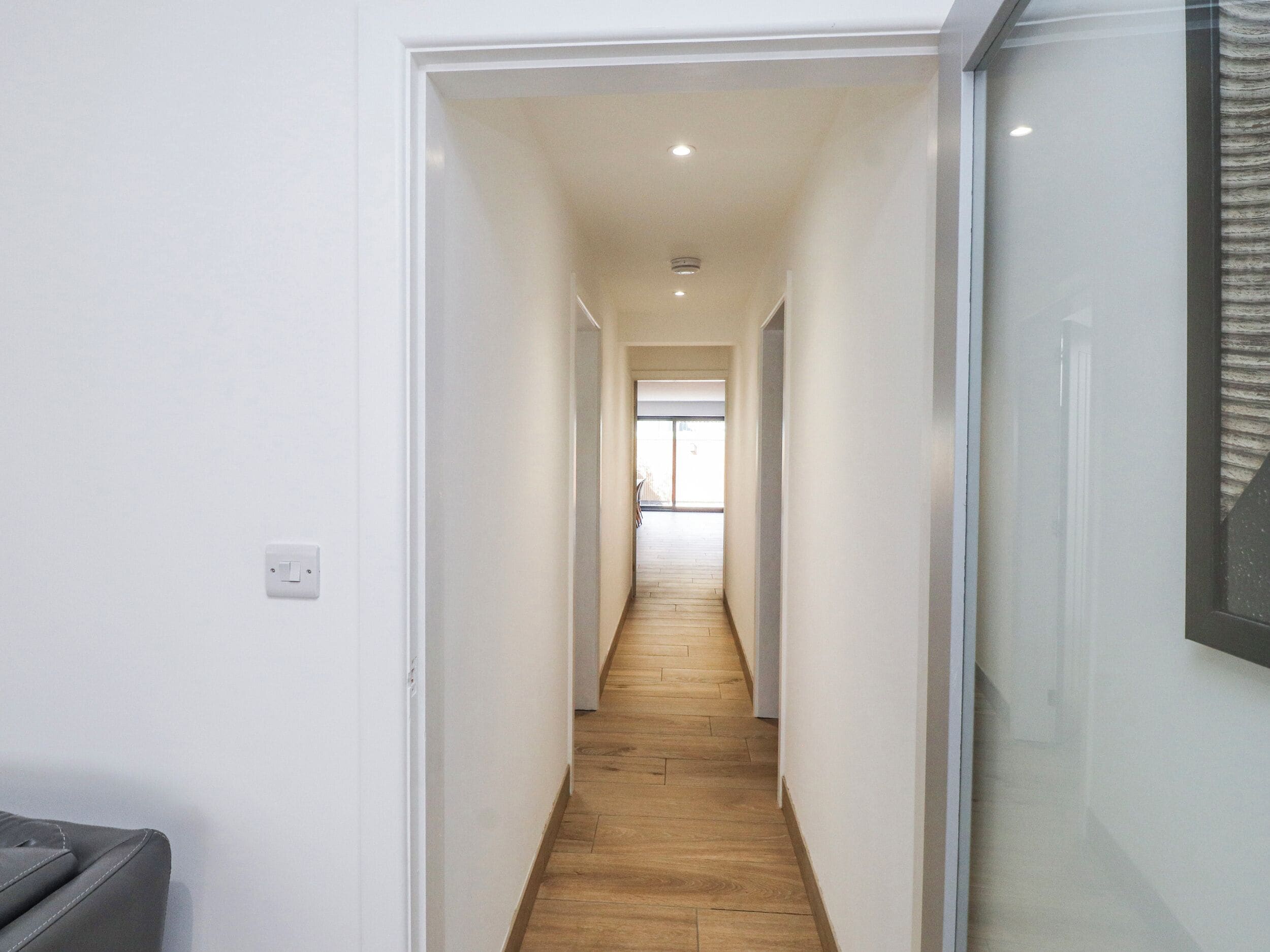 A narrow hallway with wooden flooring, white walls, and a door at the end.