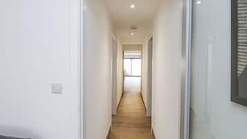 A narrow hallway with wooden flooring, white walls, and a door at the end.