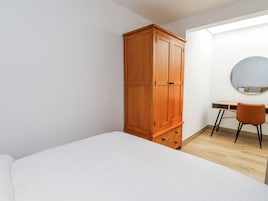 Un dormitorio con cama, armario de madera, escritorio con silla y espejo redondo en la pared.