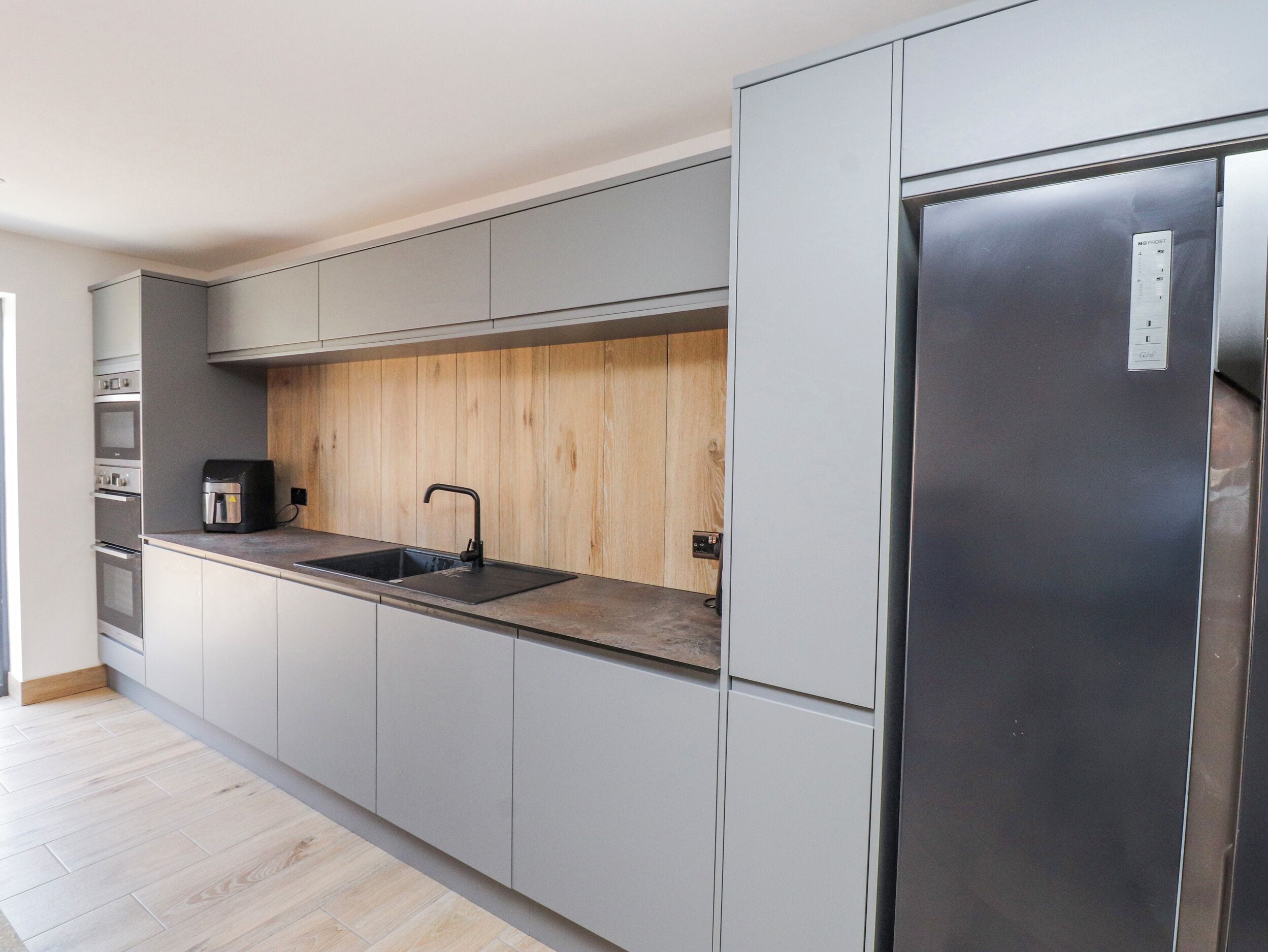 Una cocina moderna con armarios grises, un protector contra salpicaduras de madera, un refrigerador de acero inoxidable y una cafetera.