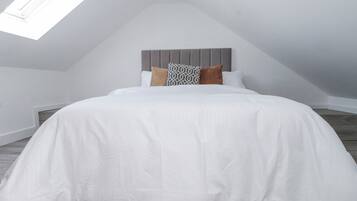 Un dormitorio con cama, cabecera, almohadas y tragaluz.