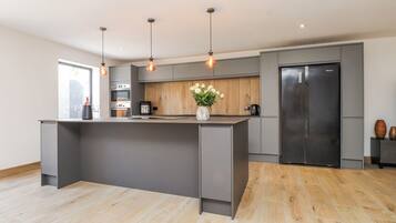 Een moderne keuken met een centraal eiland, inbouwapparatuur, hanglampen en een houten spatwand.