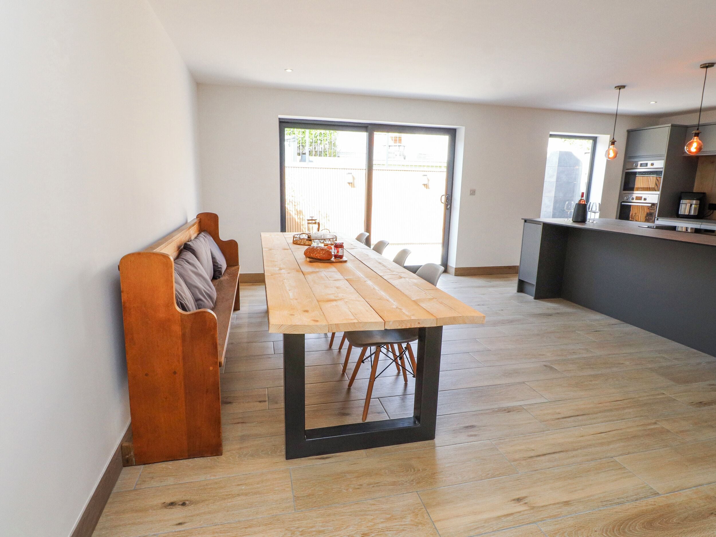 Una cocina moderna con una mesa y banco de madera, una puerta corrediza de vidrio y una pequeña isla con pileta.
