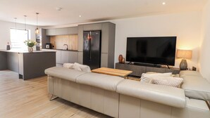 A modern living room with a sofa, a TV, and a kitchen area. - Bigting (Rhosneigr)