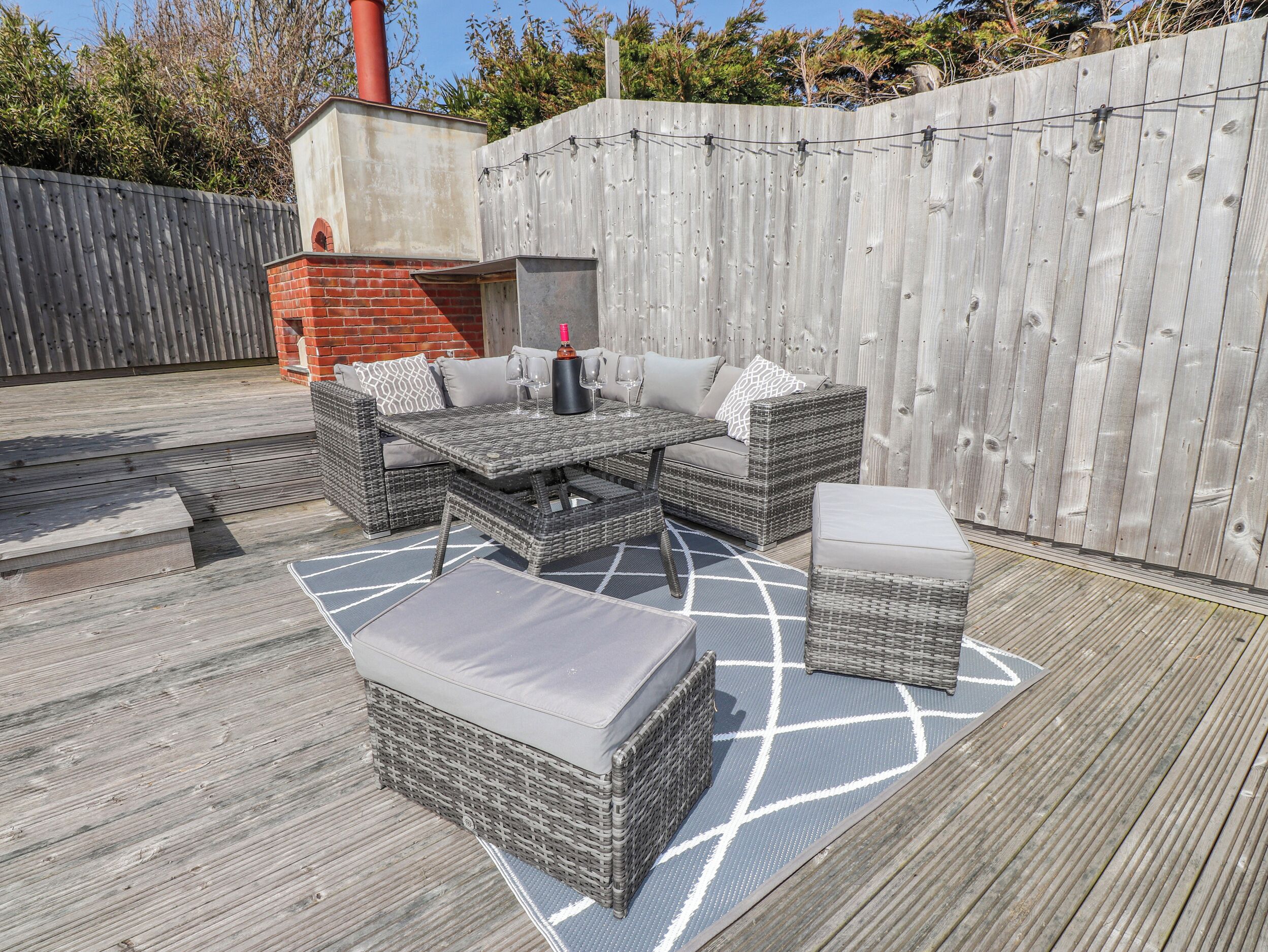 Eine Terrasse im Freien mit Korbmöbeln, einem Backofen aus Ziegelsteinen und einem Holzboden.