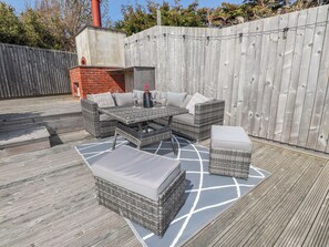 Un patio al aire libre con mobiliario de mimbre, un horno de ladrillo y una terraza de madera.