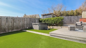 A backyard with artificial grass, a wooden deck, and a barbecue area. - Bigting (Rhosneigr)