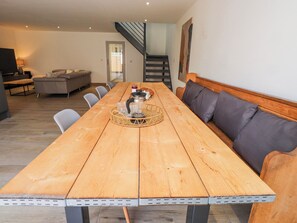 A long wooden dining table with a woven basket centerpiece, grey upholstered benches, and a staircase in the background. - Bigting (Rhosneigr)