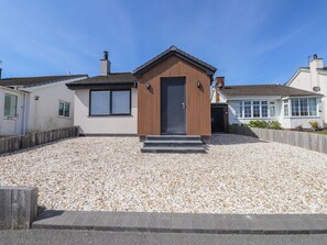 A modern house with a gravel driveway, a wooden front door, and a small porch. - Bigting (Rhosneigr)