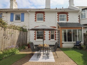 A patio with a table and chairs, a wooden fence, and a house with red brick and white walls. - Hares Cottage (Torquay)
