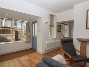 A spacious living room with a large window, a radiator, a wooden floor, and a grey armchair. - Hares Cottage (Torquay)