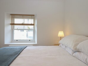 A bedroom with a bed, a window with blinds, a bedside lamp, and a radiator. - Hares Cottage (Torquay)