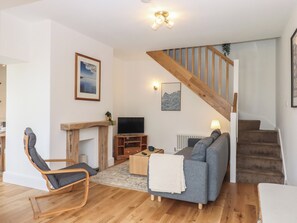 A living room with a wooden chair, a sofa, a TV, a fireplace, and a staircase. - Hares Cottage (Torquay)