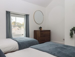 Ein Zimmer mit zwei Betten, einem Schminktisch, einem Spiegel und einem Fenster mit Vorhängen.