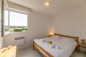 A bedroom with a bed, a bedside table, a nightstand, a window with a view, and a ceiling light. - Apartment with terrace in Carcans (Carcans)