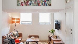 Ein modernes Wohnzimmer mit Stadtbildgemälde, einer Couch, einem Couchtisch, einer Lampe und einem Fernseher.