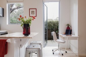Une cuisine moderne avec un plan de travail en bois, un vase rouge orné de fleurs, un tableau encadré accroché au mur et une porte-fenêtre coulissante donnant sur un balcon.