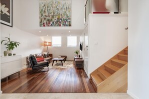 Un salon spacieux avec un escalier en bois, un ensemble de canapés, une table basse et un grand tableau abstrait.