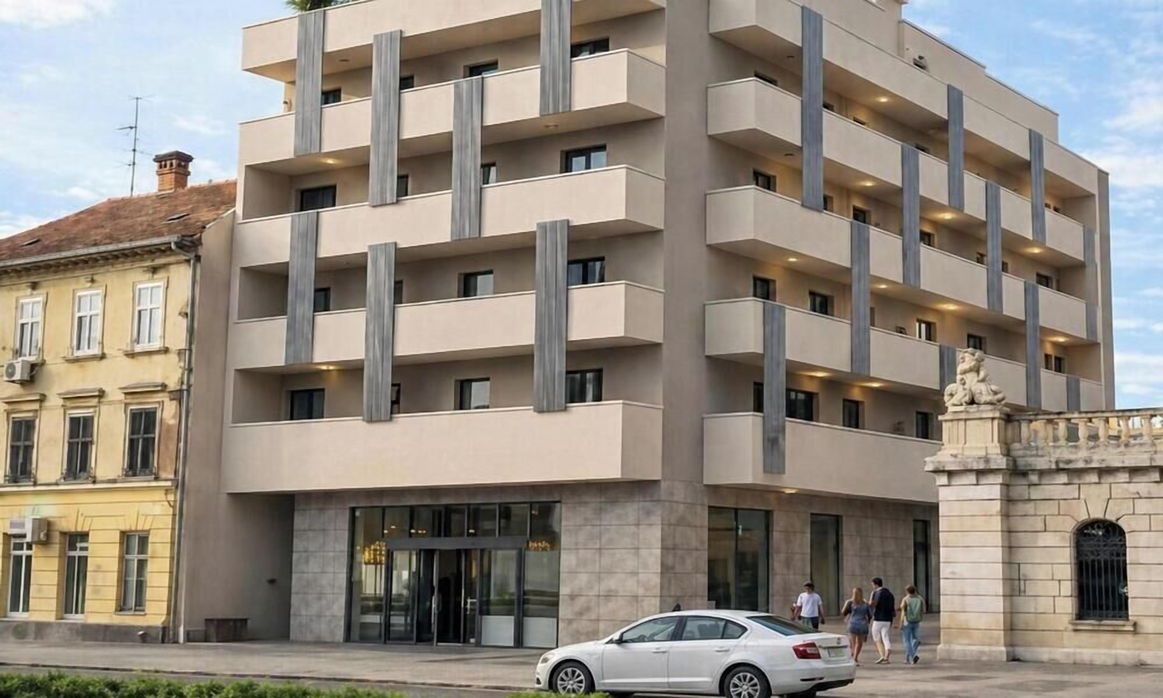 A multi-story hotel with a modern design, featuring balconies, a central entrance, and a stone facade.
