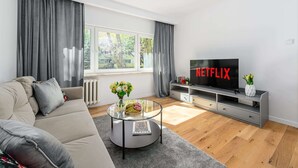 Uma sala de estar moderna com um sofá, uma mesa de centro de vidro, uma televisão e uma estante de livros.