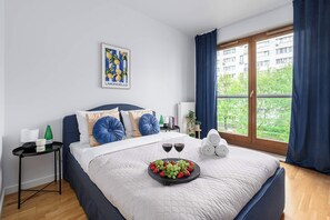 Un dormitorio con una cama, una bandeja de fruta, dos copas de vino tinto y vistas al exterior.