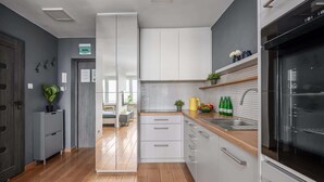 A modern kitchen with wooden flooring, white cabinets, a built-in oven, and a window overlooking the dining area. - Lumina apart near the Visla embankment (Warszawa)