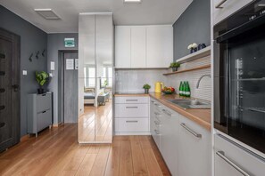 A modern kitchen with wooden flooring, white cabinets, a built-in oven, and a window overlooking the dining area. - Lumina apart near the Visla embankment (Warszawa)