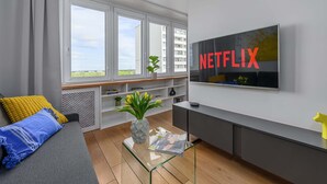 A modern living room with a large window, a sofa, a coffee table, a TV mounted on the wall, and a bookshelf. - Lumina apart near the Visla embankment (Warszawa)