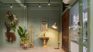 Una habitación con pared verde, un espejo, una planta decorativa, una estatua y una puerta que da a una vista exterior.