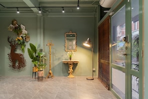 A room with a green wall, a mirror, a decorative plant, a statue, and a door with a view of the outside. - Baan La-Or Heritage Suite (Bangkok)