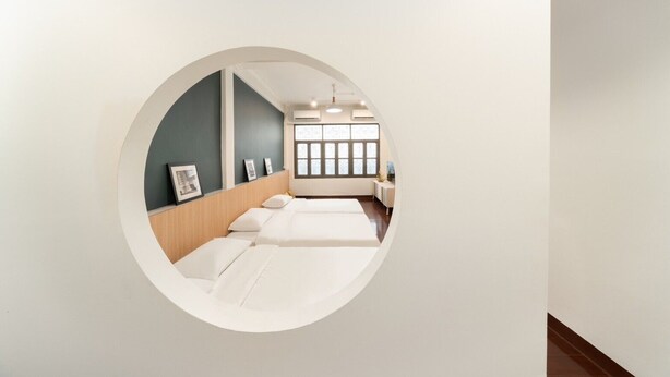Vista circular desde una ventana de una habitación de hotel, con cama, mesita de noche y persianas.