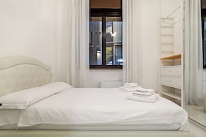 Ein ordentlich gemachtes Bett mit Kopfteil, ein Fenster mit Vorhängen, ein Nachttisch und ein Kleiderschrank mit Spiegel.