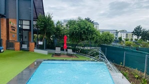 Una piscina con un deck perimetral, una sombrilla roja y un edificio con un letrero que dice 'LIFESTYLE CENTER'.