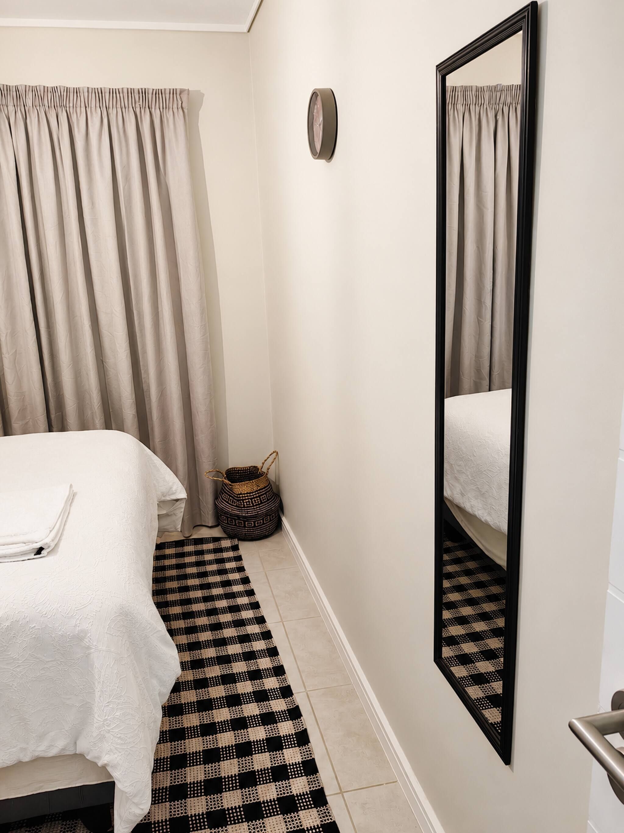 Een slaapkamer met een bed, een spiegel, een vloerkleed en een klein geweven mandje.