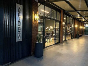 A restaurant with a metal exterior, glass doors, and indoor seating visible through the windows.