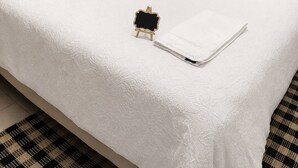 A neatly made bed with white bedding and pillows, a black headboard, and a small wooden easel with a blank canvas.