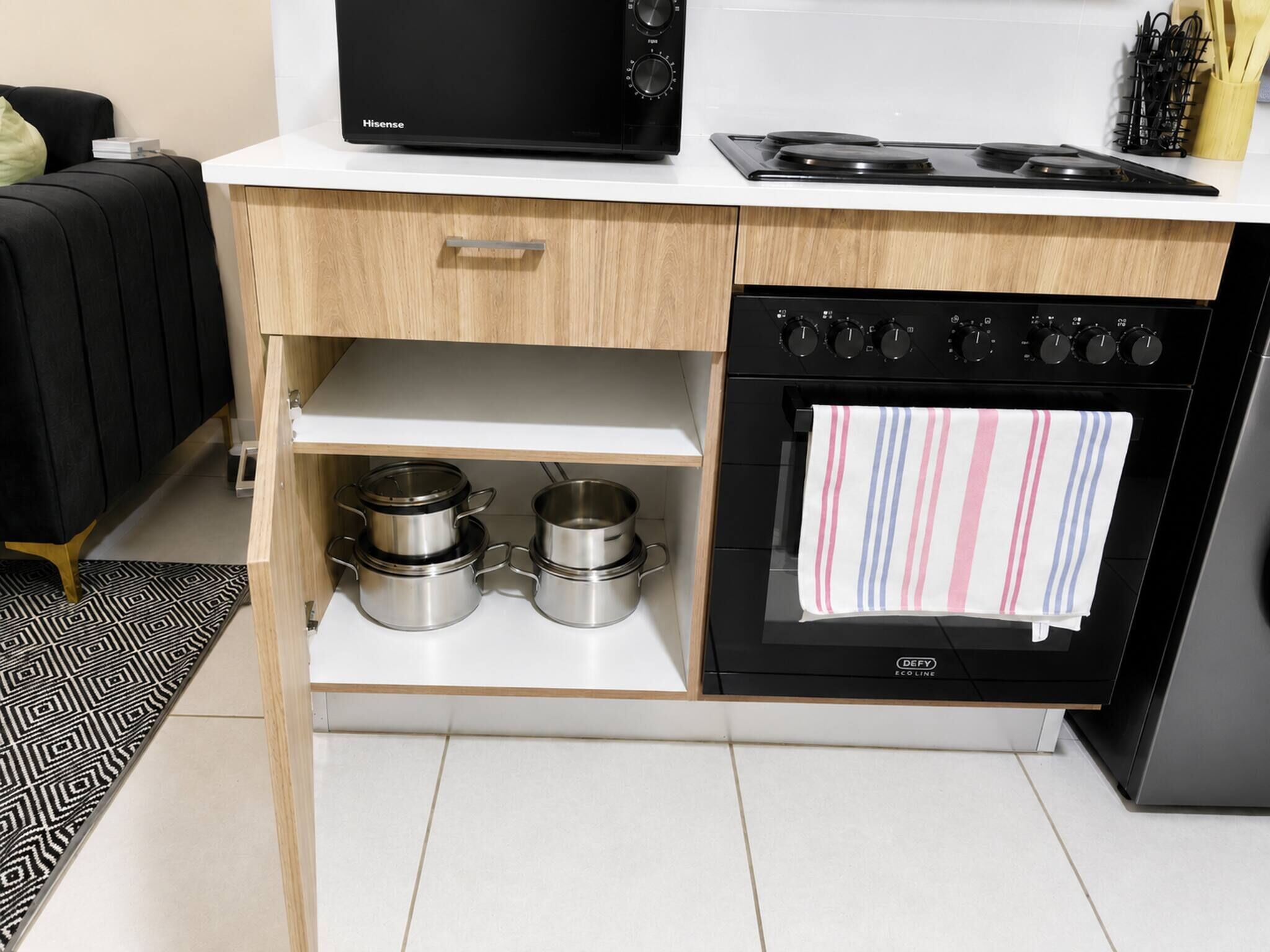Una cocina con microondas, estufa, horno y dos ollas de acero inoxidable sobre un estante de madera.