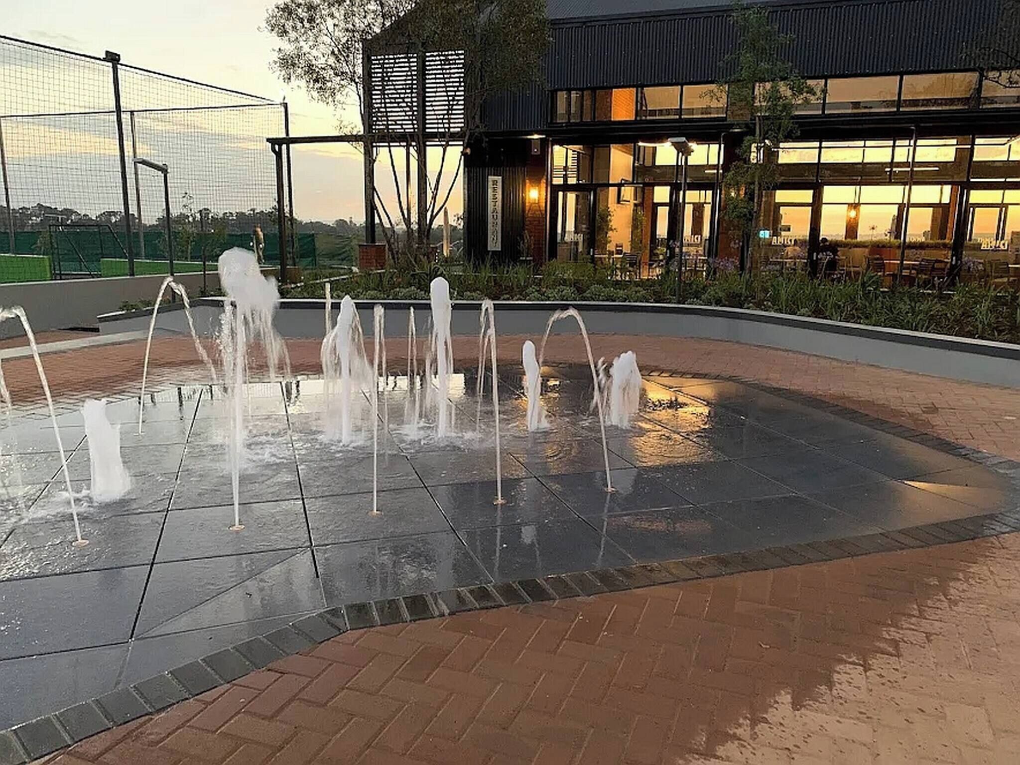 Uma fonte com vários jatos, rodeada por um espaço pavimentado com borda de tijolos.