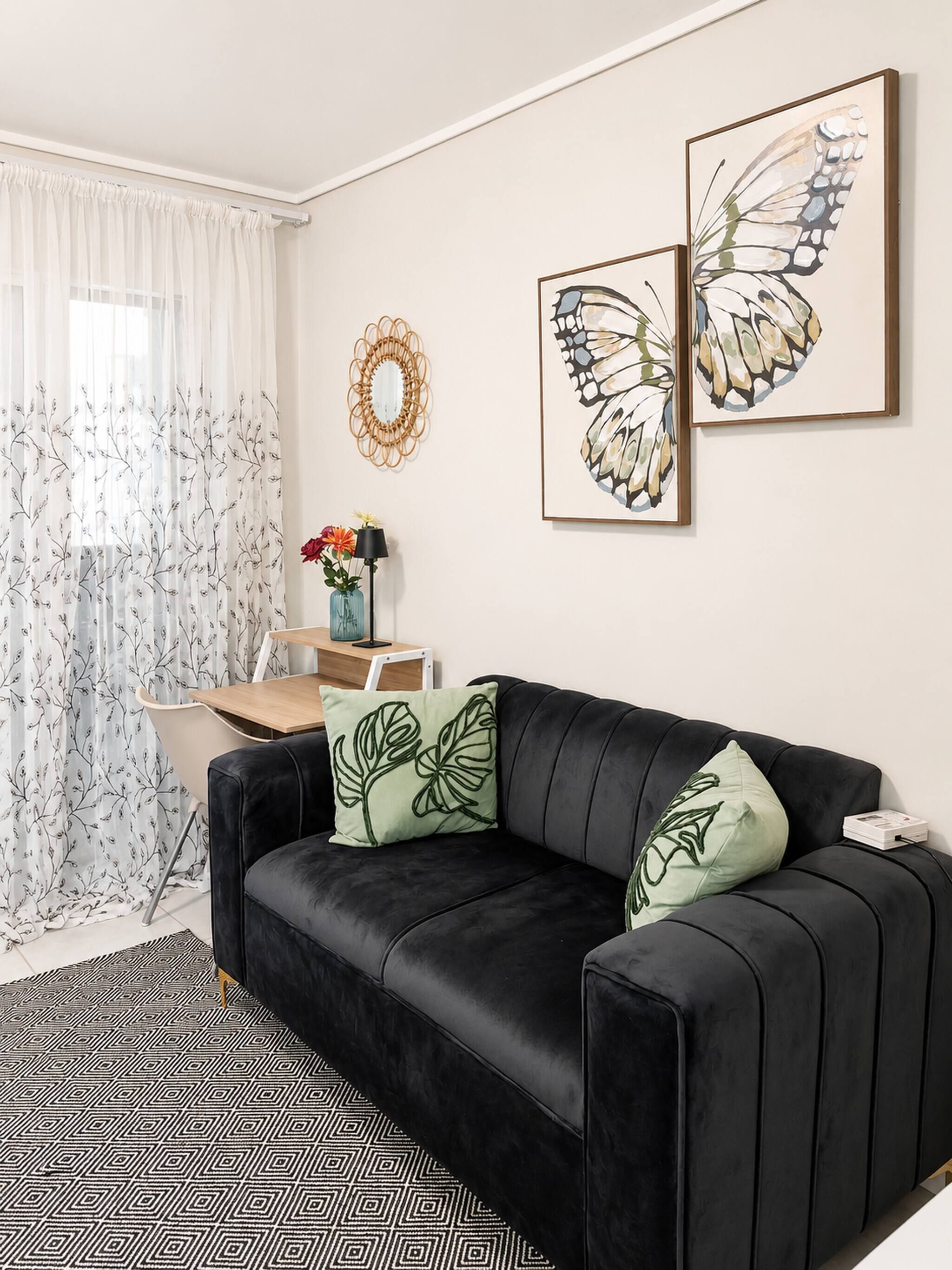 A modern living room with a black leather sofa, a patterned rug, a dining table with chairs, and two framed butterfly artworks on the wall.