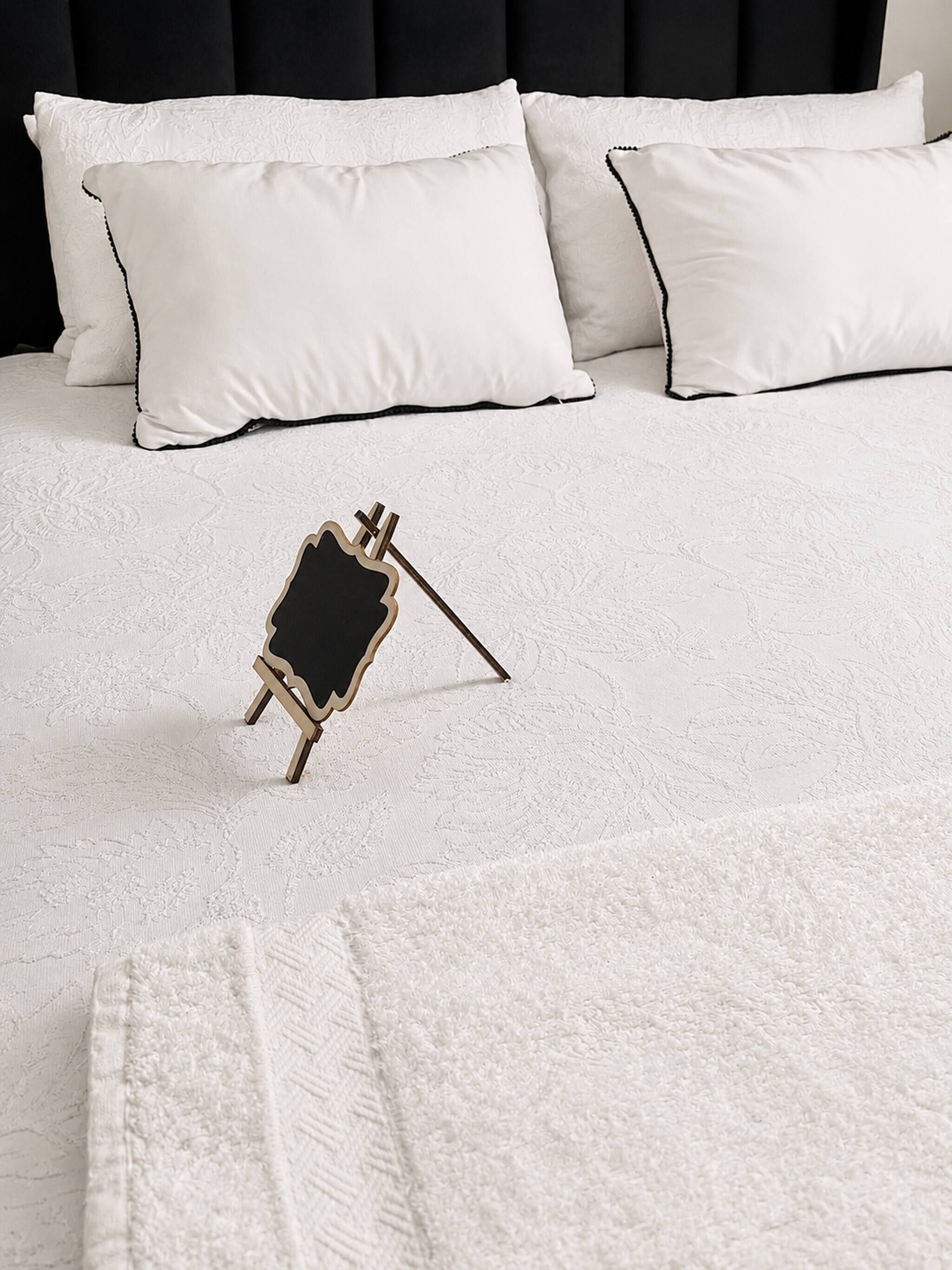 A bed with white bedding and a small black and gold object on it.