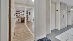 Eine moderne Hotelhalle mit Holzboden, einem Essbereich mit Stühlen und Tisch sowie einem Flur mit den nummerierten Türen 12.