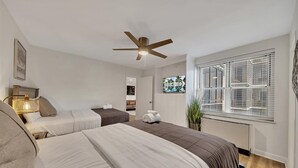 Ein Hotelzimmer mit zwei Betten, einem Deckenventilator, einem Fenster mit Jalousien und einer Pflanze.