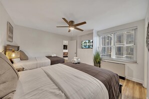 A hotel room with two beds, a ceiling fan, a window with blinds, and a plant. - Modern Twist in a Historic Building, sleeps 6 (Atlanta)