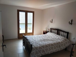 A bedroom with a bed, a nightstand, a lamp, a window with blinds, and a door. - Family home in the mountains, in the Ossau Valley (Béost) (Béost)