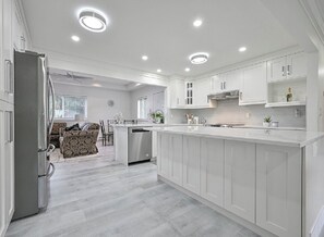 A modern kitchen with white cabinetry, a central island, and recessed ceiling lights. - Fully Furnished House, Delta, BC, Canada, (Delta)